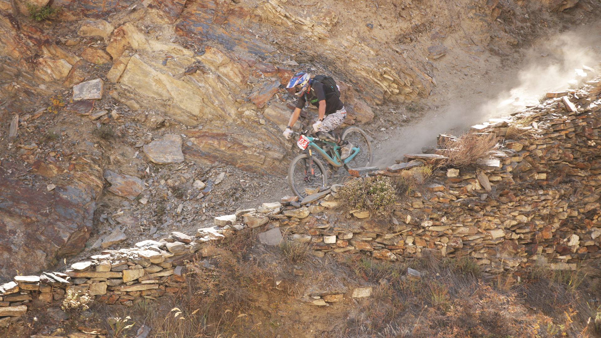 A rider descends a stone walled switchback trail above a village
